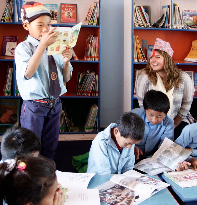 A team member from Raven Supply smiles while watching a 5th grade child reading from a school book